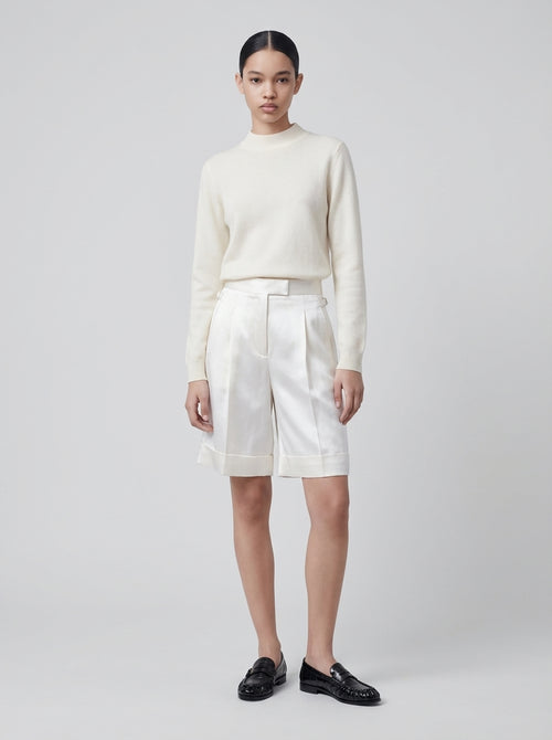 Model trägt ivoryfarbenen Cashmere Pullover mit Halbrollkragen und weißer Shorts